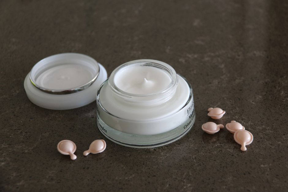Open jar of luxurious face cream with capsules on a dark textured surface for skincare routines.